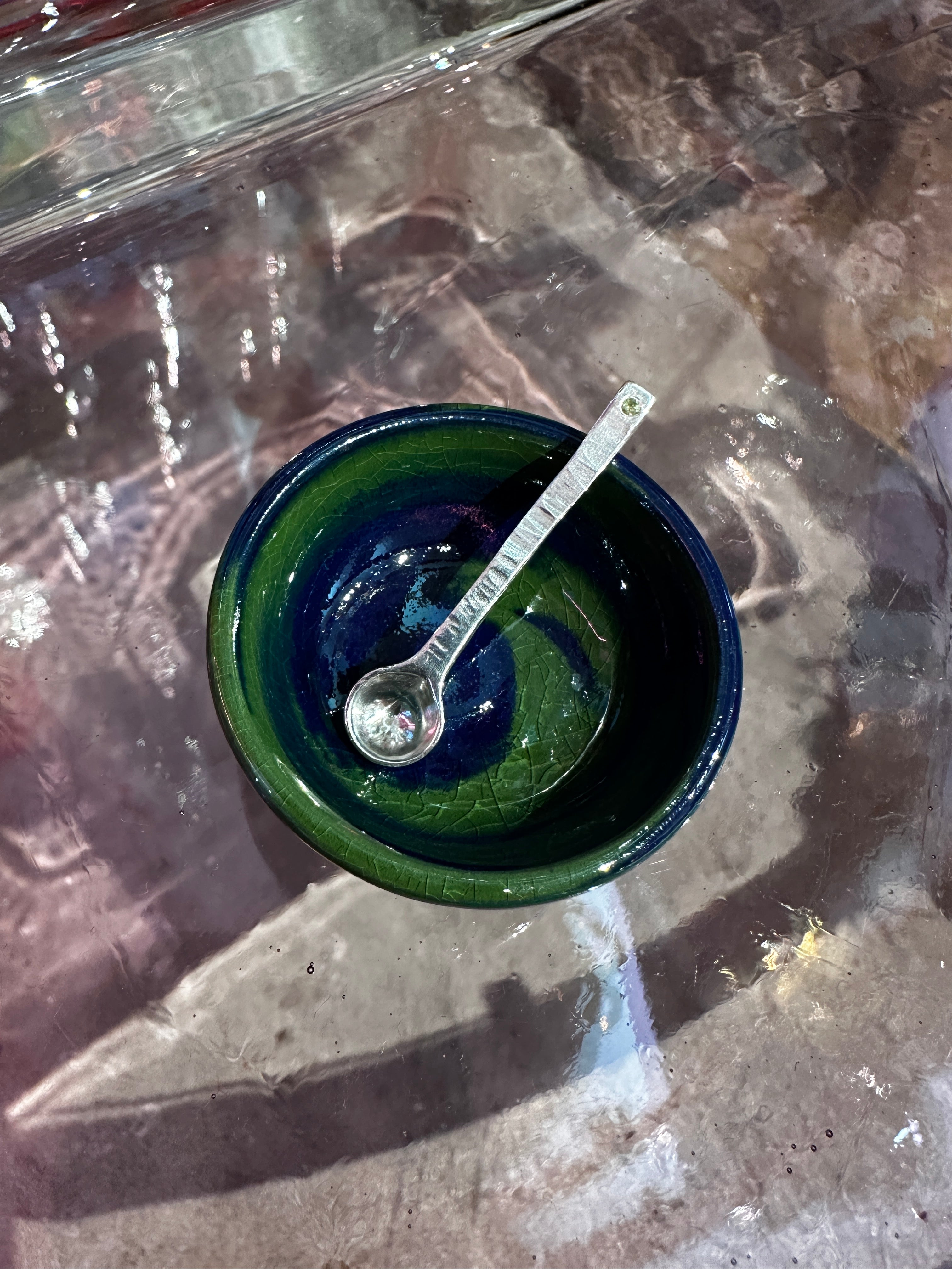 Blue and green ceramic bowl with silver salt spoon on a reflective surface
