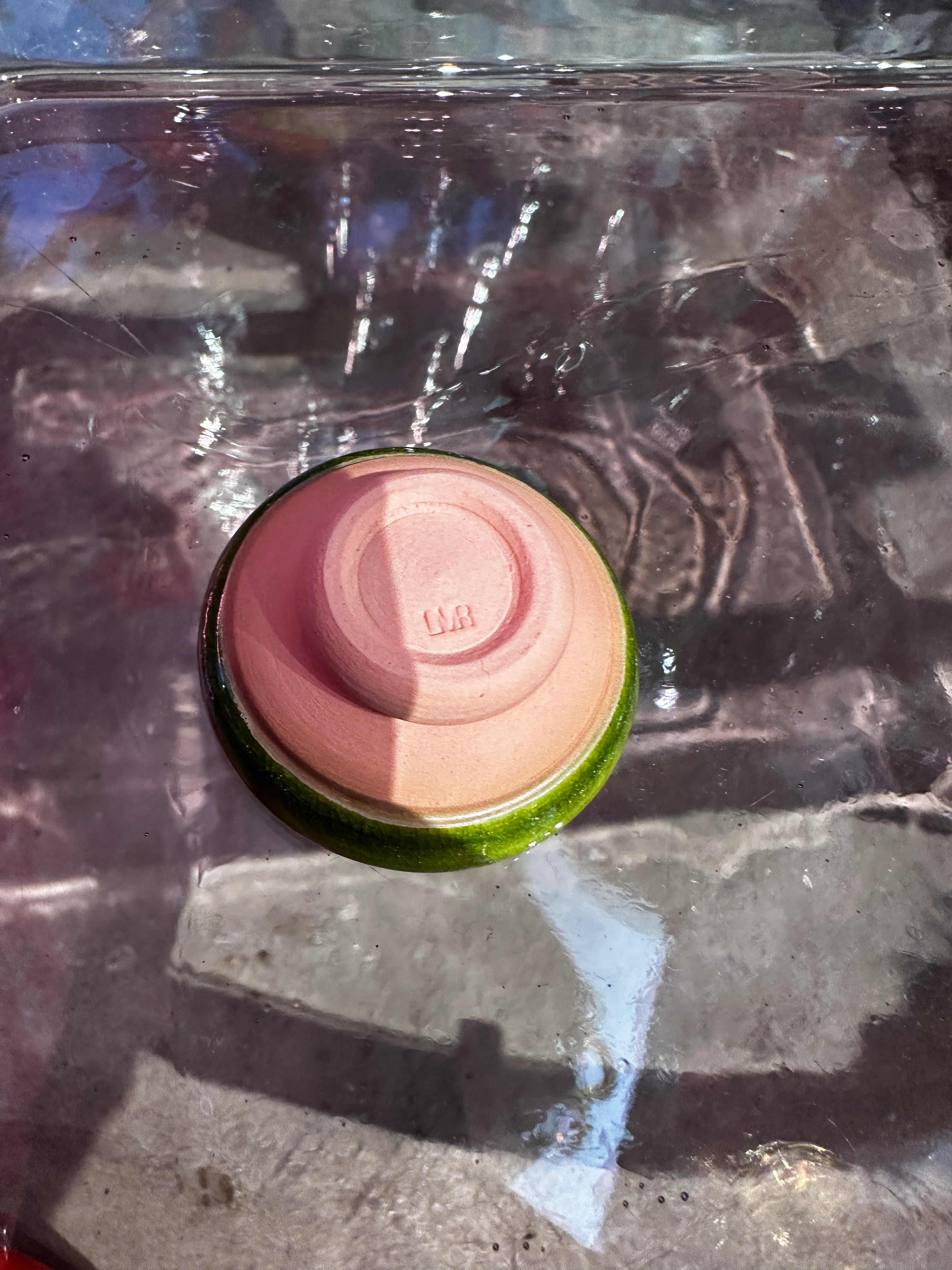 Bottom view of pink and green ceramic pot on reflective surface