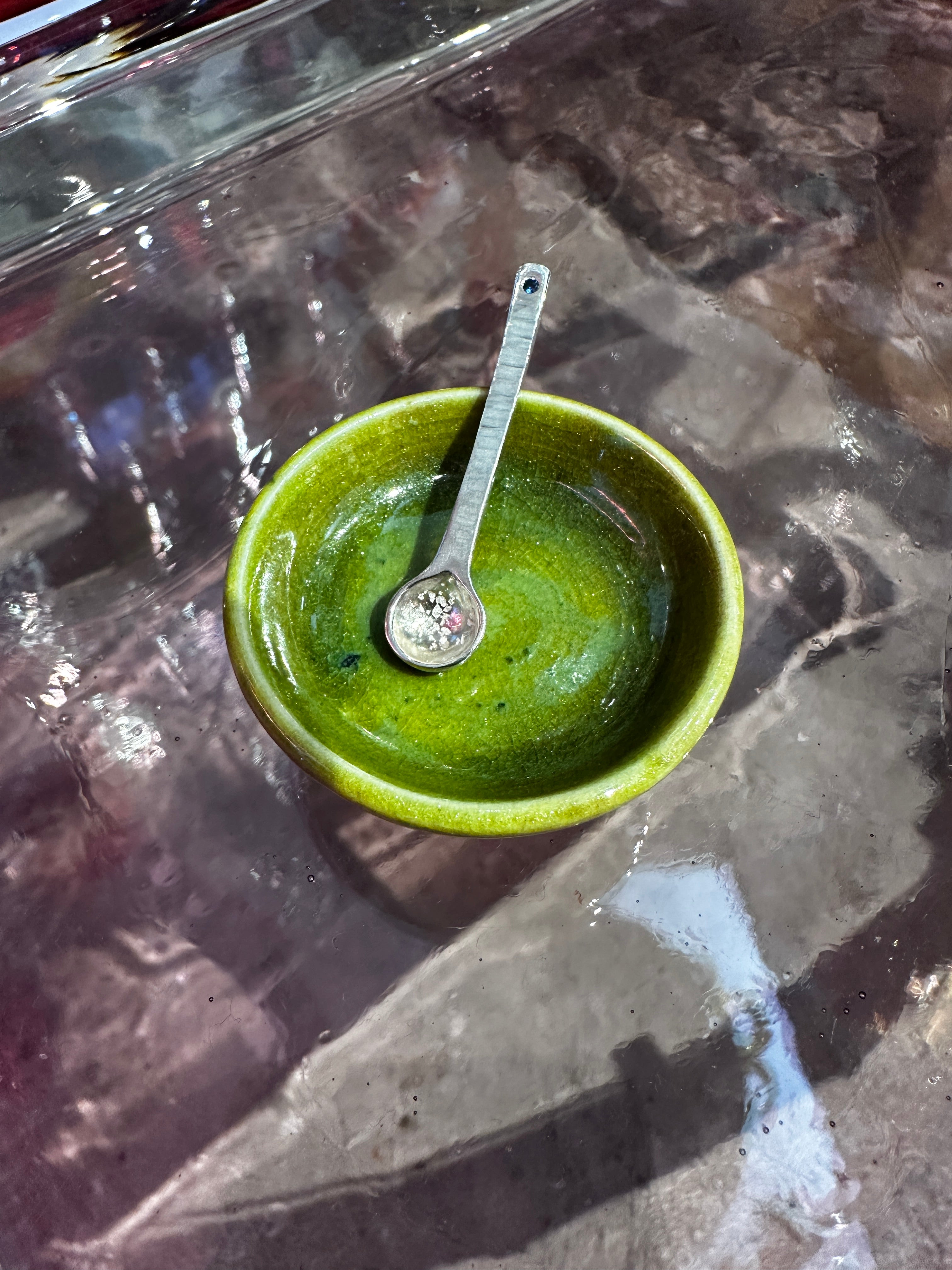 Silver salt spoon in green ceramic bowl on reflective surface