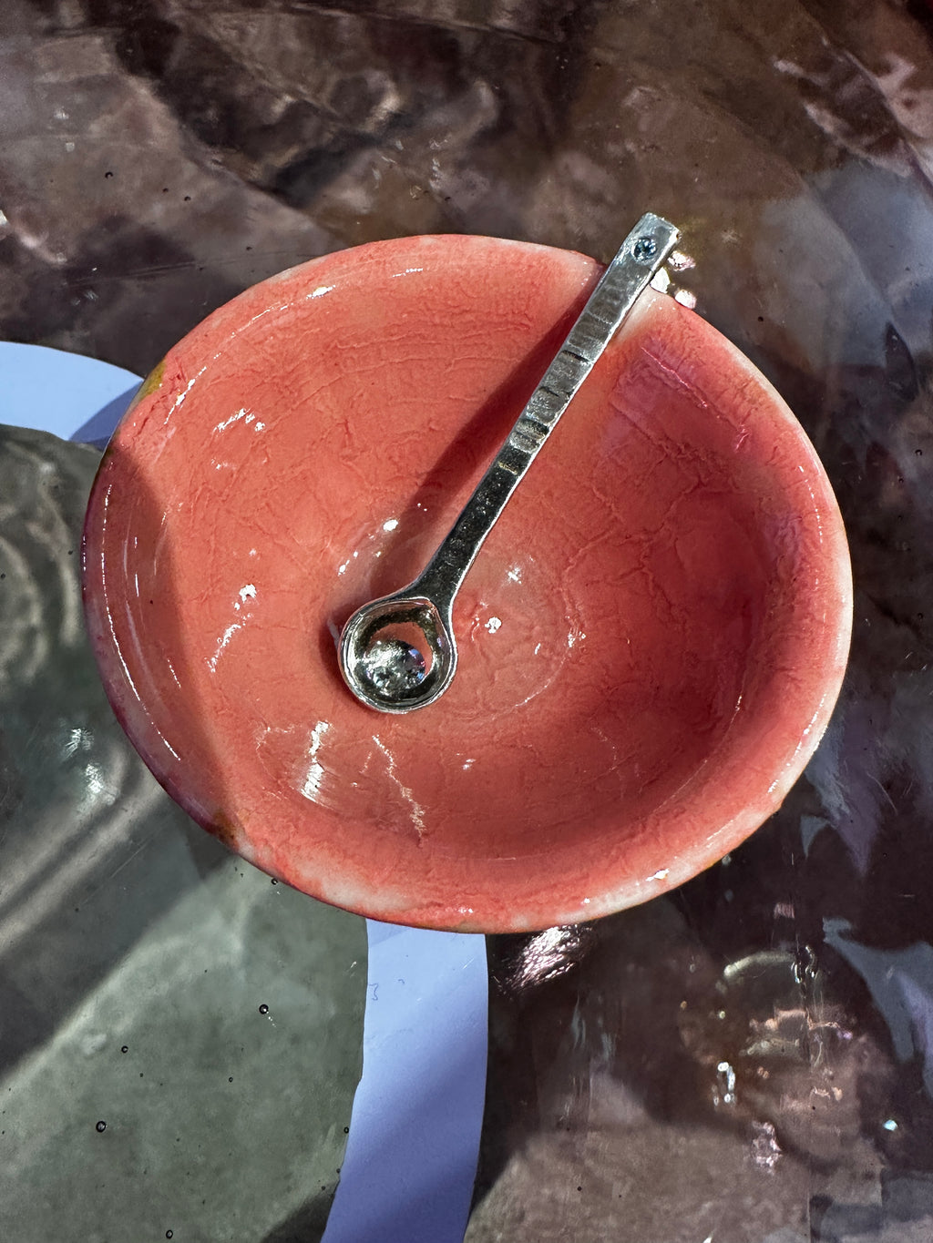 Silver salt spoon in a pink ceramic bowl with a reflective surface