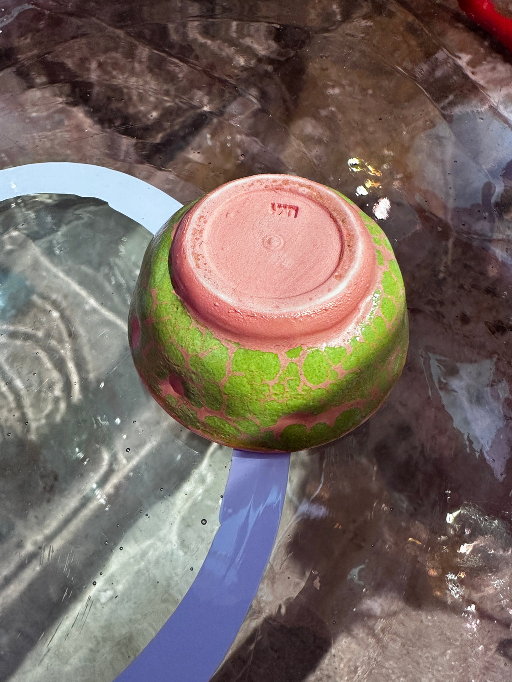 Bottom of green and pink ceramic bowl on a reflective surface