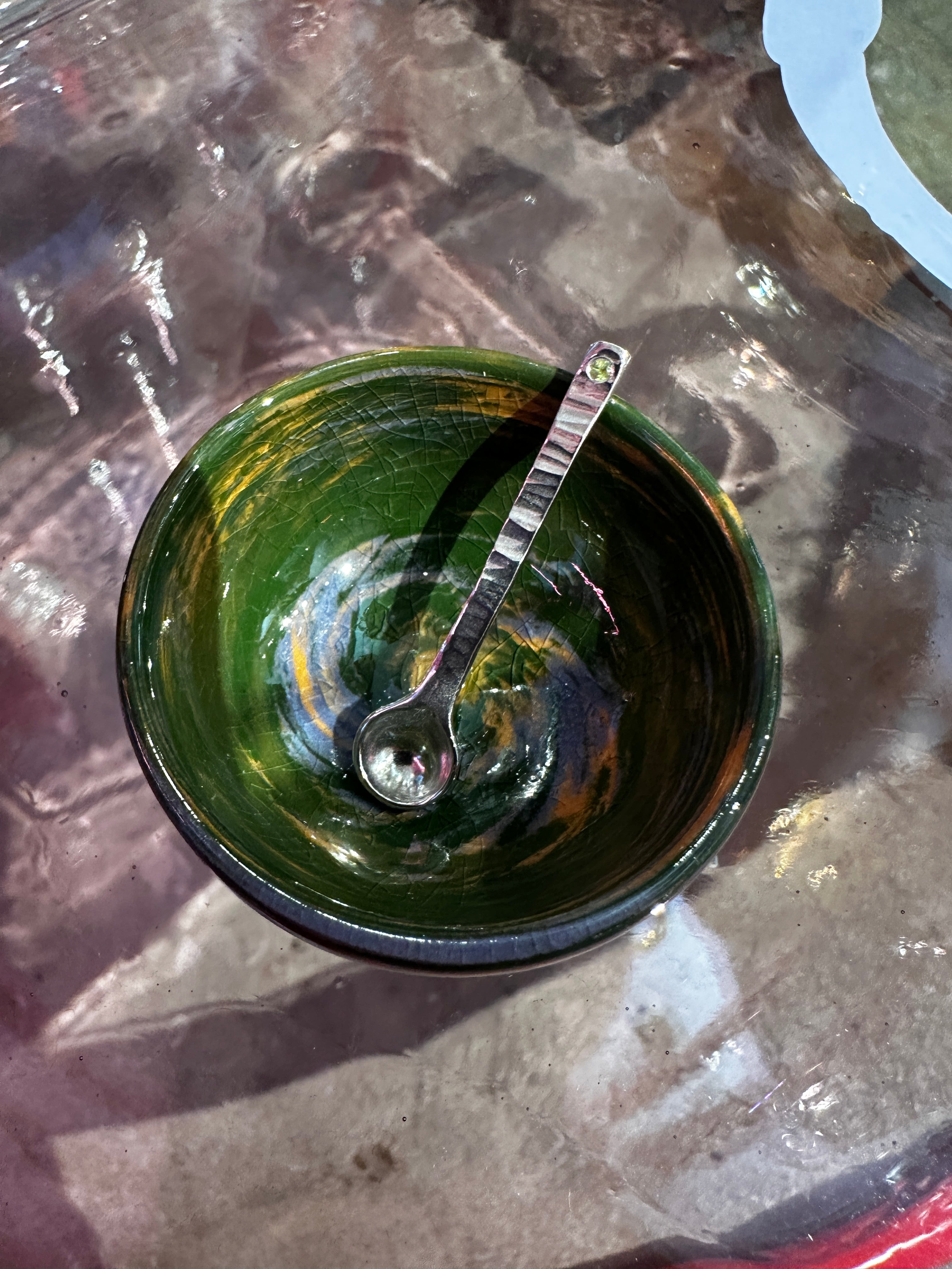 Green ceramic bowl with a spoon on a reflective surface