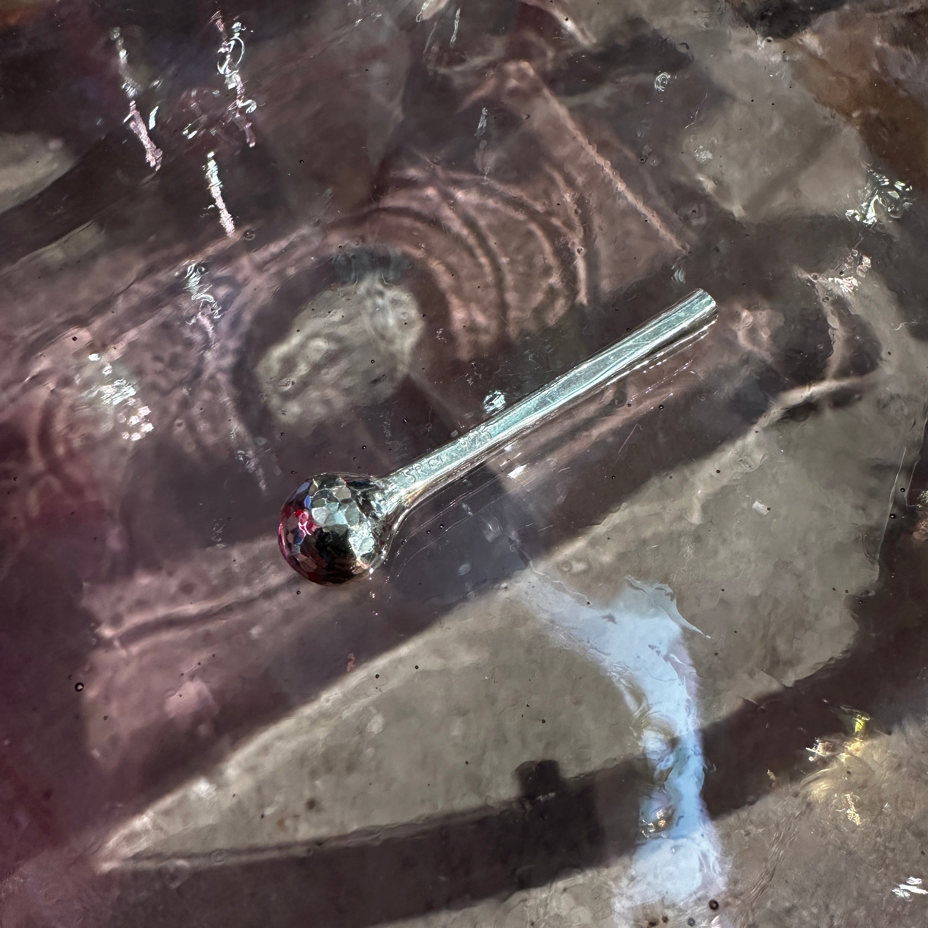 Silver salt spoon on a textured surface with reflection
